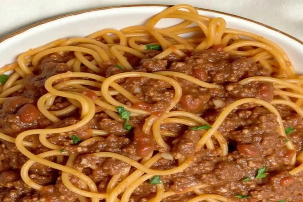 Plate of spaghetti bolognese with grated Parmesan and fresh basil.