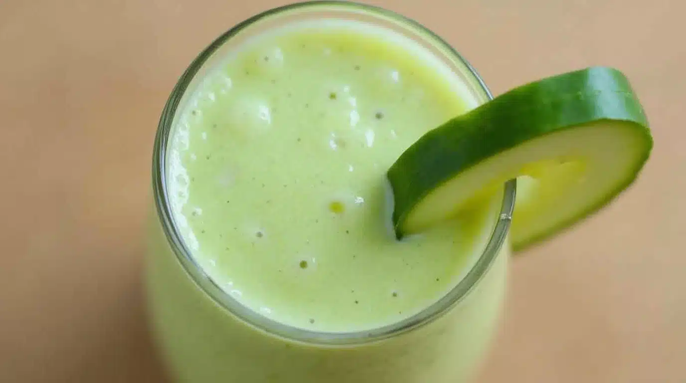 A vibrant glass of cucumber and pineapple smoothie on a countertop.