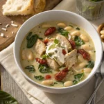 "Steaming bowl of creamy Tuscan chicken soup with kale, white beans, and sun-dried tomatoes, garnished with Parmesan and basil."