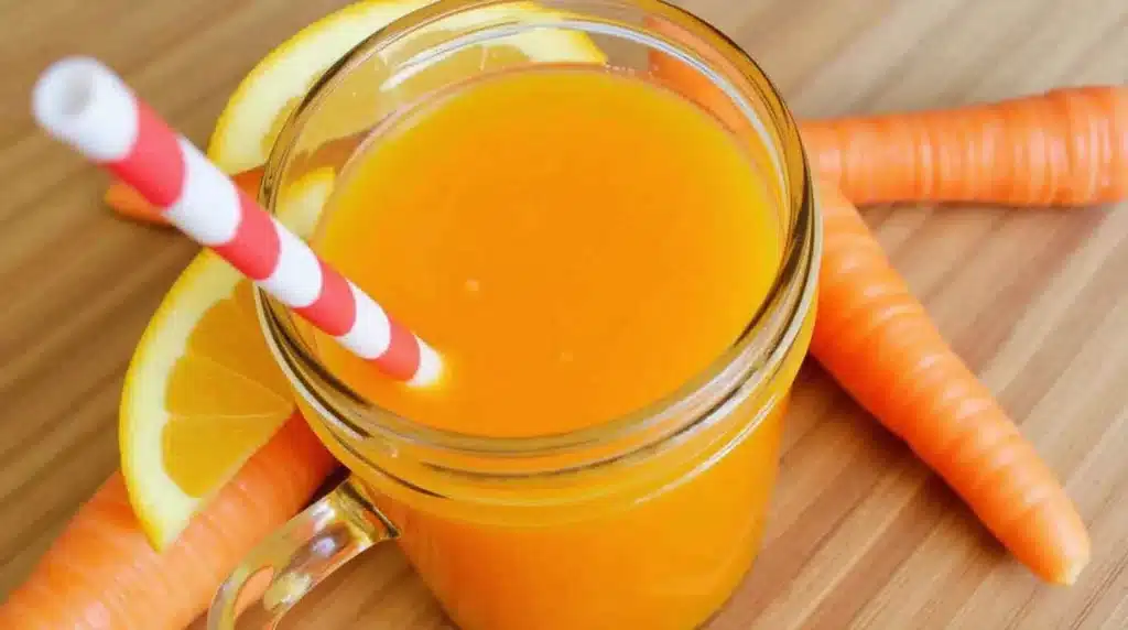 A glass of freshly made carrot juice recipe with fresh carrots nearby.